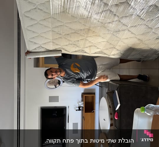 אדם מחזיק מזרן עטוף בניילון